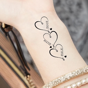 Puede incluir: Tres corazones entrelazados con los nombres "Noah", "Mamá" y la fecha "11.06.20" dentro de cada corazón. Dos corazones pequeños se encuentran en la parte inferior del diseño.