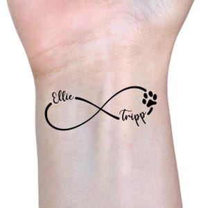 Puede incluir: Tatuaje temporal negro con un símbolo de infinito con los nombres "Ellie" y "Tripp" en cursiva. Una huella de pata está incorporada en el diseño, simbolizando una mascota.