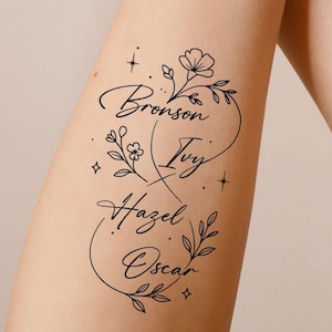 Puede incluir: Un diseño de tatuaje floral negro con los nombres Bronson, Ivy, Hazel y Oscar en escritura cursiva. El diseño incluye detalles florales y de hojas, junto con pequeños detalles de estrellas y cuadrados. El tatuaje está en un brazo.