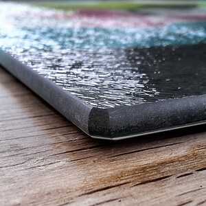 May include: Close-up of the edge of a black glass cutting board with a textured surface. The board is sitting on a wooden surface.