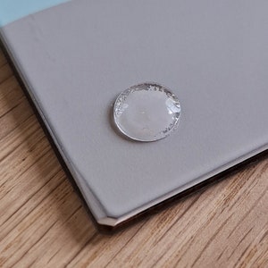 May include: A clear, round, adhesive sticker with a slightly textured surface.