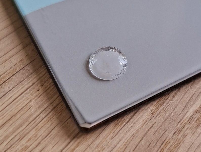 May include: A clear, round, adhesive sticker with a slightly textured surface.