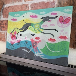 May include: A glass cutting board with a colorful illustration of three greyhounds running through a field of flowers and butterflies. The background is a light blue with pink clouds.