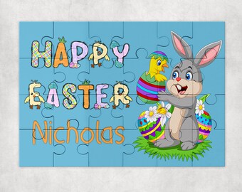 May include: A blue jigsaw puzzle with the words "HAPPY EASTER Nicholas" in colorful letters. The puzzle features a cartoon bunny, a chick hatching from an egg, and decorated Easter eggs on a green patch.