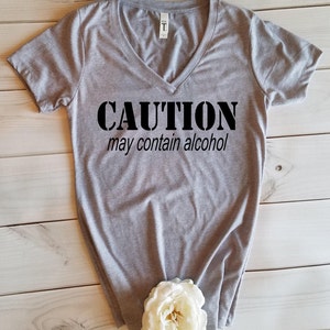 May include: Gray V-neck t-shirt with the text "CAUTION may contain alcohol" printed in black.