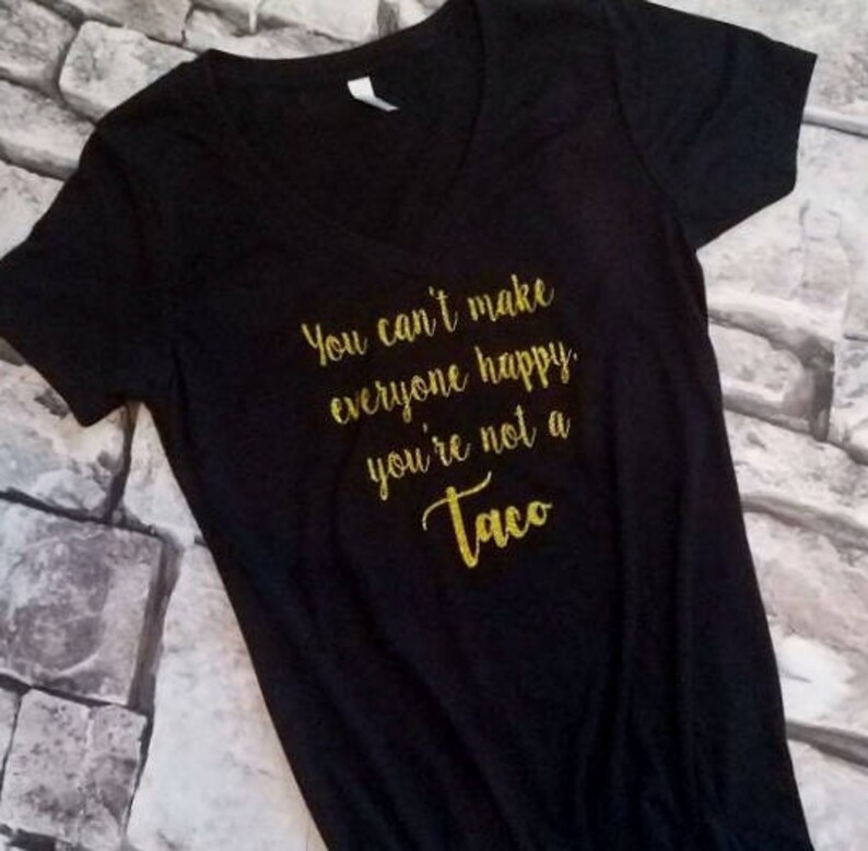 May include: Black V-neck t-shirt with gold glitter text. The text reads "You can't make everyone happy you're not a Taco". The shirt is made of a soft material and is suitable for casual wear.