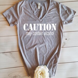 May include: Gray V-neck t-shirt with the text "CAUTION may contain alcohol" printed in white.