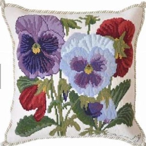 May include: A square decorative pillow with a detailed needlepoint design of pansies in shades of purple, red, and blue. The flowers are set against a white background, with green leaves and stems. The pillow has a rope trim.