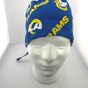 May include: A blue surgical scrub cap featuring the Los Angeles Rams logo in yellow and white. The cap is made of fabric and is designed to be worn during medical procedures or in a professional setting.