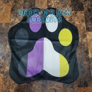 May include: Black paw-shaped flag featuring non-binary pride colours: purple, white, and yellow. The flag has the text "DRAGON'S DEN FURSUITS" in a blue and white font.