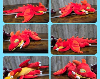 May include: A plush red dragon toy with orange wings, horns, and yellow underbelly. The dragon has white claws and a friendly expression. The toy is lying on a wooden surface.