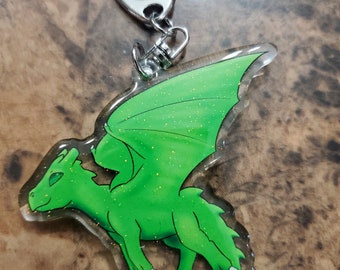 May include: Green glitter dragon keychain with a silver metal key ring. The dragon is flying with its wings spread out.