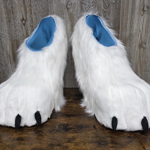 May include: A pair of white furry paw slippers with black claws and a blue interior. These novelty slippers are designed to resemble animal paws and are made of soft, plush material.