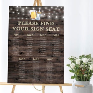 May include: A rustic wooden sign with string lights, a beer and a baby bottle illustration, and the text "PLEASE FIND YOUR SIGN SEAT". The sign lists names and table numbers for a wedding reception.