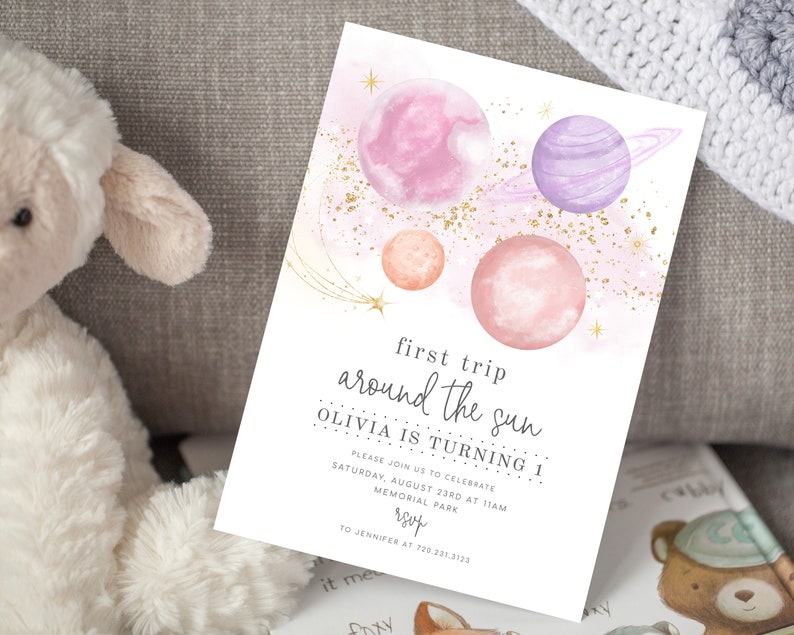 May include: A pink and white watercolour invitation with a gold glitter background. The invitation features planets and stars and the text "first trip around the sun Olivia is turning 1".