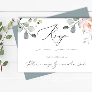 May include: A white RSVP card with a floral design featuring pink roses and eucalyptus leaves. The text "RSVP" is written in cursive script. The card includes lines for guests to indicate whether they will attend, unable to attend, and the number attending. The card also includes the text "Please RSVP by November 23rd."
