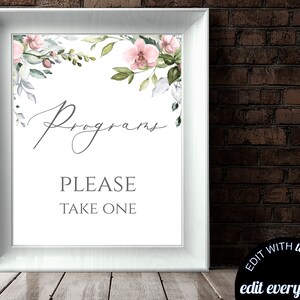 May include: A framed white sign with the word "Programs" in elegant script, and the text "PLEASE TAKE ONE" in a simple font. The top of the sign is decorated with watercolor floral elements in pink, green, and white. The sign is displayed on a wooden surface.