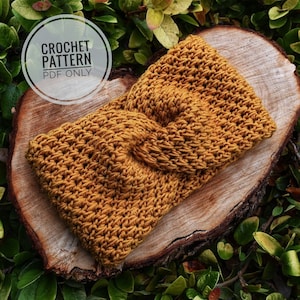 May include: A crocheted headband in a mustard yellow color. The headband is twisted and has a knot in the center. The headband is on a wooden surface.