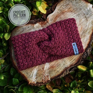 May include: A maroon crocheted headband with a knotted design. The headband has a small silver tag with the text "=S&D=".