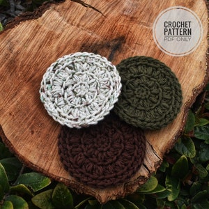 May include: Three crocheted coasters in different colors: white with green flecks, dark green, and brown. The coasters are on a wooden surface.