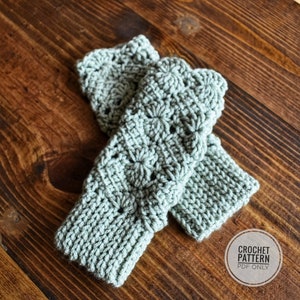 Könnte beinhalten: Ein Paar gehäkelte Fingerlose Handschuhe in hellgrün. Die Handschuhe haben ein Spitzenmuster und werden auf einer Holzoberfläche gezeigt. CROCHET PATTERN PDF ONLY steht in weißer Schrift auf einem schwarzen Kreis.