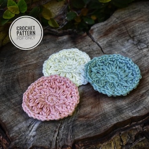 May include: Three crocheted cotton rounds in different colours: pink, light green, and cream. The rounds are on a wooden surface.