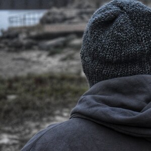 May include: A person wearing a dark gray hooded sweatshirt and a dark gray knitted beanie.