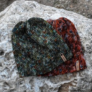 May include: Two knitted hats with a colorful, speckled pattern. The hats are made with a soft yarn and have a unique, hand-crafted look. The hats have leather tags with the text "S&D" on them.