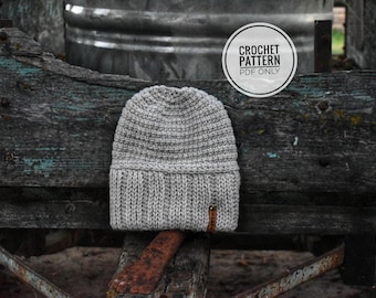 May include: A gray crocheted beanie hat with a ribbed brim and a small brown leather tag. The hat is displayed on a rustic wooden surface. A circular graphic reads "CROCHET PATTERN PDF ONLY".