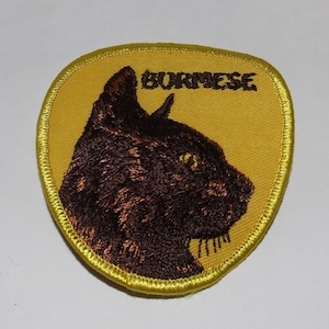 Op de afbeelding: Geborduurde patch met een bruin kattenprofiel met gele ogen op een gele achtergrond. Het woord "BURMESE" is boven de kat geborduurd. De patch heeft een gele gestikte rand.