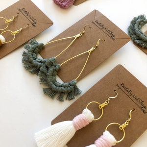 May include: Assortment of handmade tassel earrings displayed on brown card stock with the text "KnotsByNelshop" printed on each card. The earrings feature a variety of colours and styles, including green, white, pink, and gold.