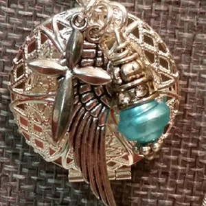 May include: A silver locket necklace with a delicate filigree design. The locket features a silver angel wing charm, a silver cross charm, and a blue glass bead charm.