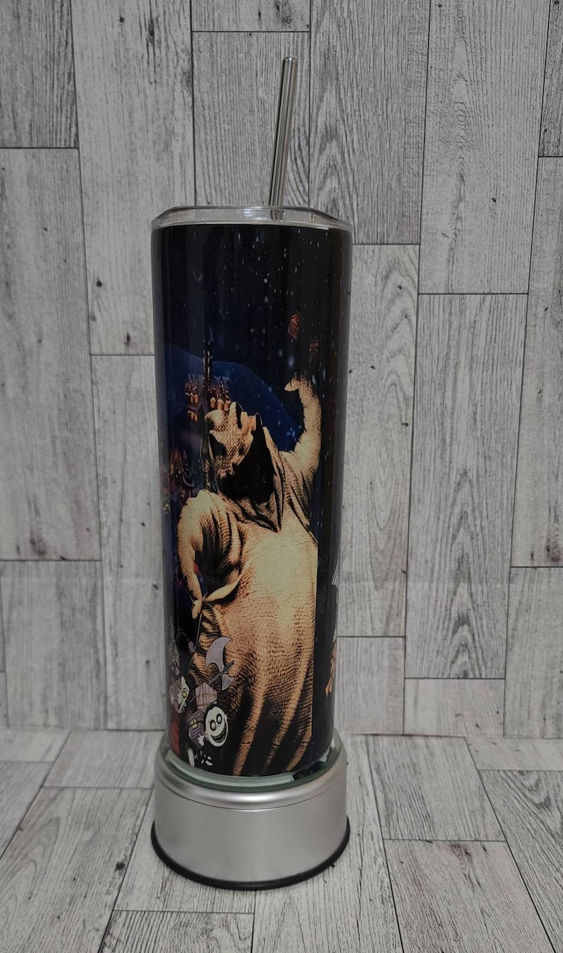 Puede incluir: Un vaso de acero inoxidable con una imagen en blanco y negro de Jack Skellington de Pesadilla antes de Navidad. El vaso tiene una tapa plateada y una pajita.