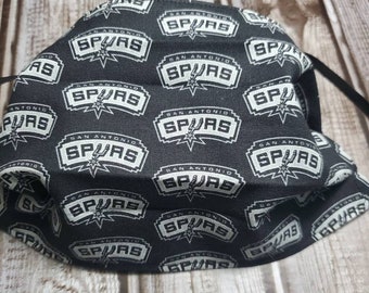 May include: Black face mask with a white repeated pattern of the San Antonio Spurs logo.