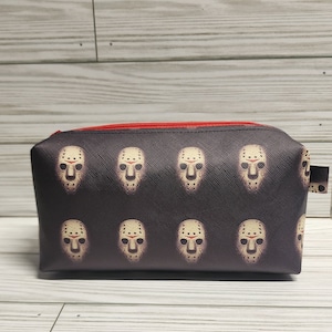 May include: A black zippered makeup bag with a repeating pattern of white hockey masks. The zipper is red.