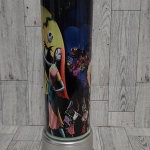 Puede incluir: Un vaso de acero inoxidable con una imagen en blanco y negro de personajes de Pesadilla antes de Navidad. El vaso tiene una tapa plateada y una base plateada.