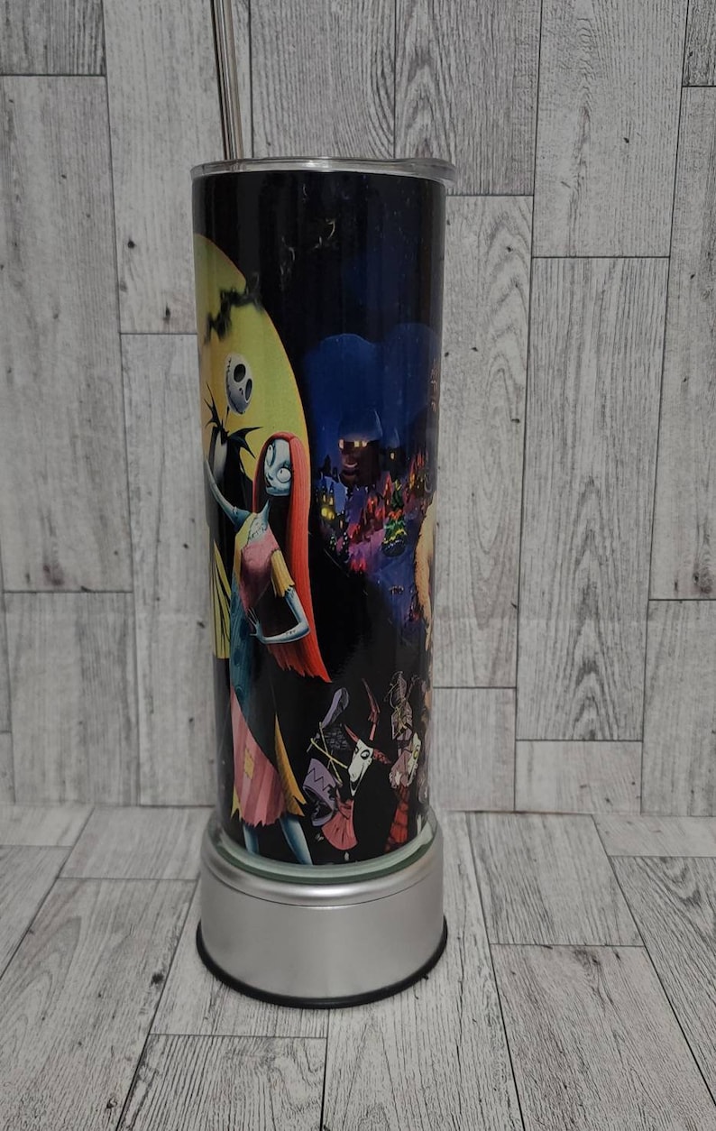 Puede incluir: Un vaso de acero inoxidable con una imagen en blanco y negro de personajes de Pesadilla antes de Navidad. El vaso tiene una tapa plateada y una base plateada.