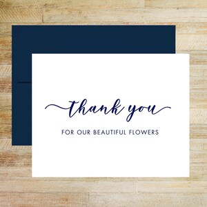 May include: A white rectangular thank you card with dark blue text that reads thank you FOR OUR BEAUTIFUL FLOWERS in a mix of script and sans-serif fonts, paired with a matching dark blue envelope positioned directly behind the card.