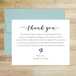 May include: A white sympathy thank you card with black text that reads: thank you, Our family wishes to express our gratitude for your gesture of sympathy and support. In our time of need, you provided a comfort that touched us deeply. With Love, The Devore Family. A small blue flower illustration is centered above the signature. The card is paired with a light blue envelope.