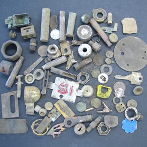 May include: A collection of various metal hardware pieces, including nuts, bolts, washers, and plates. The items are in shades of gray, silver, and brown, with some showing signs of age and wear. A few pieces have a touch of color, such as a red and white tag.