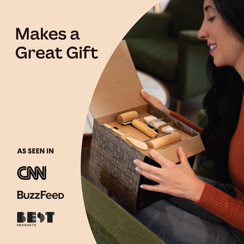 May include: A person opens a gift box containing a set of wooden tools for crafting. The box is brown with a black and white patterned design. The tools include rolling pins, a scraper, and a wooden knife.
