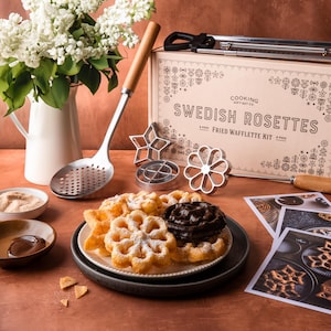May include: A set for making Swedish rosettes, a type of fried waffle. The set includes a wooden handle, a metal pan, and a box with the words "Swedish Rosettes Fried Waffle Kit".