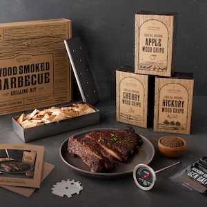 May include: A wood-smoked barbecue grilling kit with wood chips in a metal container, a grill grate, a meat thermometer, and a package of hickory sea salt. The wood chips are labeled "Apple", "Cherry", and "Hickory".