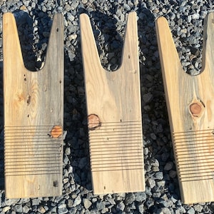 May include: Three wooden boot jacks with a rustic, weathered look. Each jack has a unique grain pattern and is made from reclaimed wood. The jacks are designed to help people put on their boots.