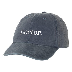May include: A dark blue denim baseball cap with the word "Doctor." embroidered in white on the front.