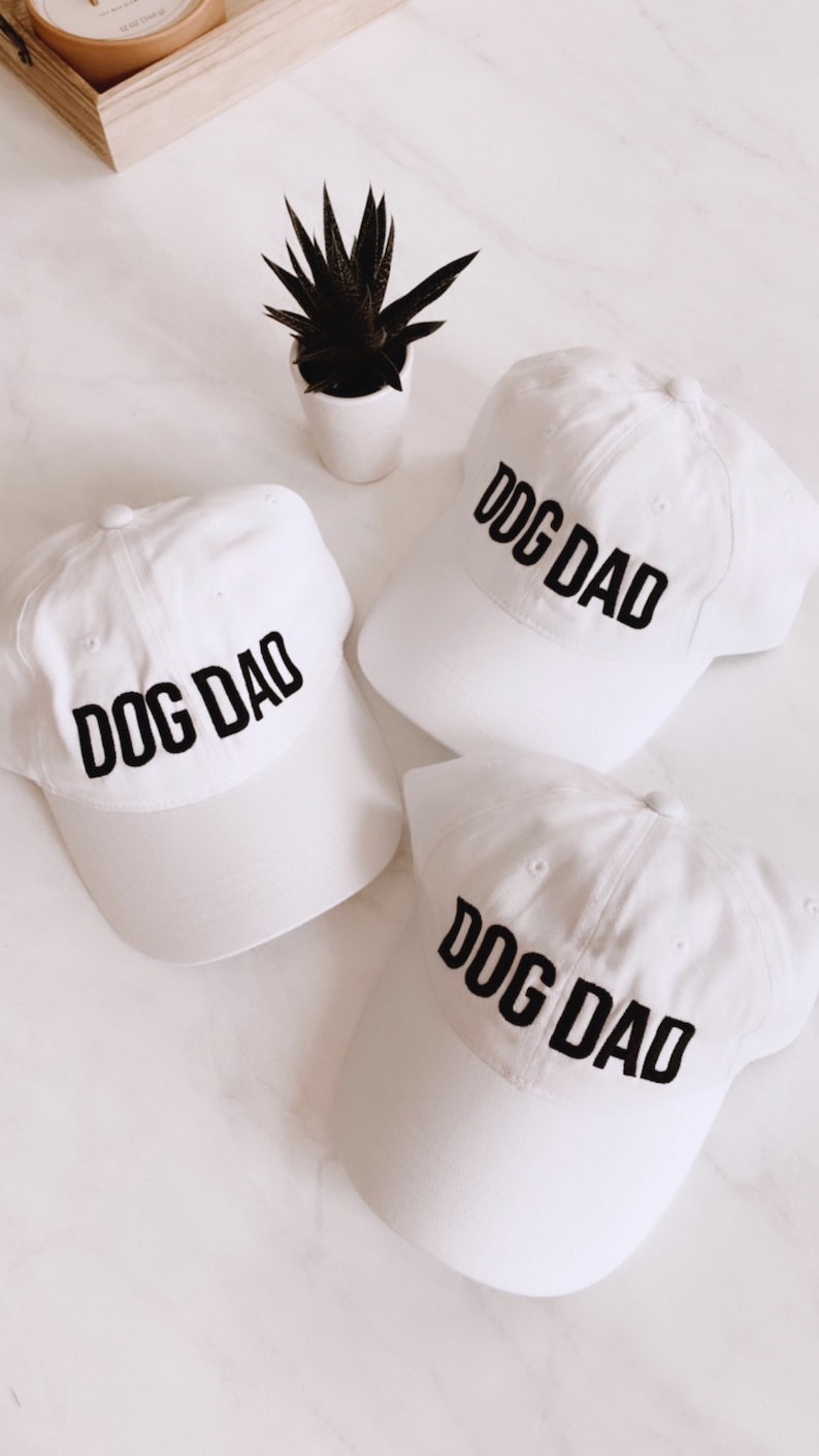 May include: Three white baseball caps with black embroidered text that reads "DOG DAD".