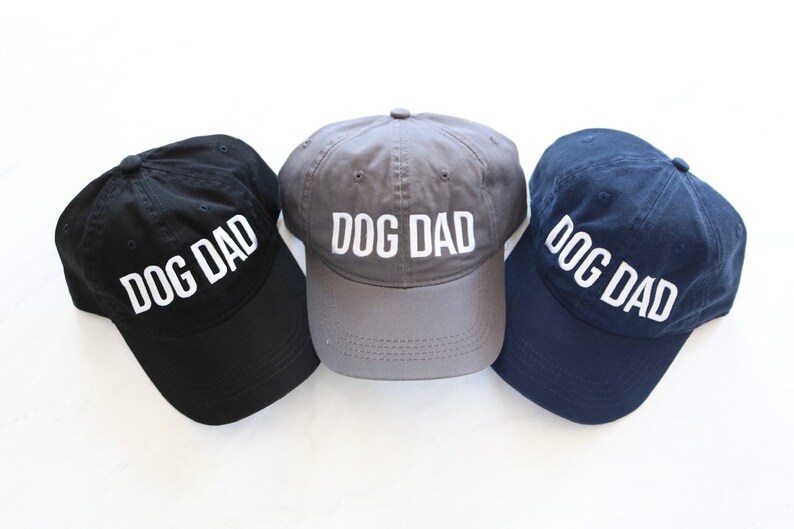 May include: Three baseball caps in black, gray, and navy blue with the text "DOG DAD" embroidered in white on the front of each cap.