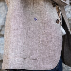 May include: A beige linen blazer with a single button closure and a pocket on the left side. The blazer has a textured weave and a subtle sheen.