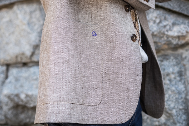 May include: A beige linen blazer with a single button closure and a pocket on the left side. The blazer has a textured weave and a subtle sheen.