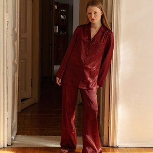 May include: A woman wearing a red and black checked pyjama set. The set includes a long-sleeved shirt and wide-leg trousers.
